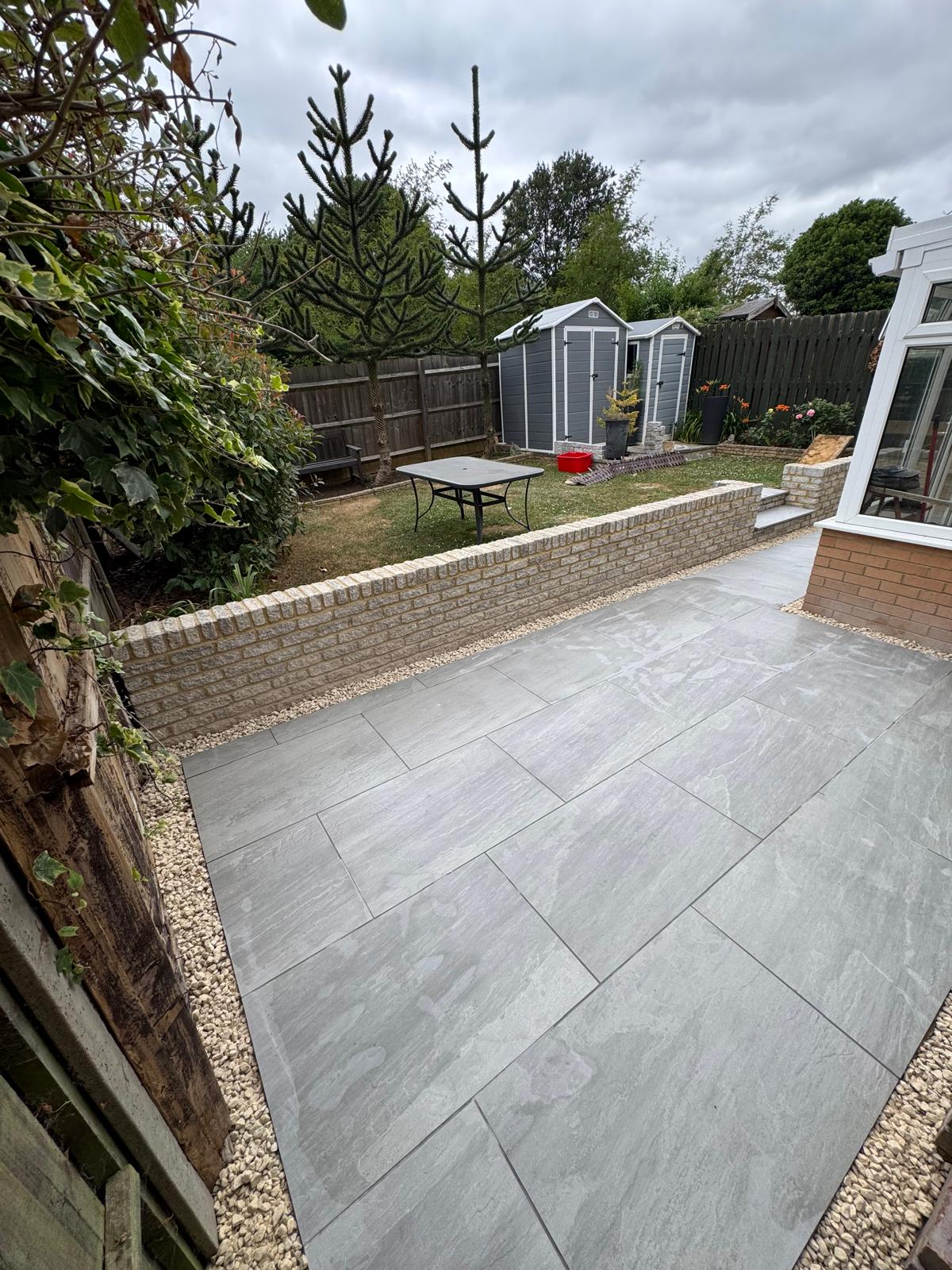 Completed grey patio beside a lawn and low garden wall
